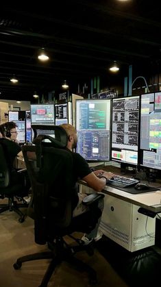 a man sitting at a desk in front of multiple computer monitors with screens on them