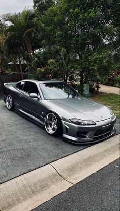 a silver sports car parked on the side of the road in front of some trees