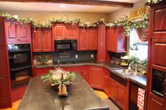 a kitchen decorated for christmas with red cabinets and green garland on the windowsills