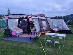 a tent is set up in the grass with chairs and tables around it for camping