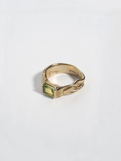 a yellow gold ring with a green stone in it's center on a white surface