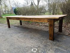 a long wooden table sitting in the middle of a park next to a white fence