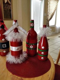 three wine bottles decorated like santa's hats and snowflakes on a table