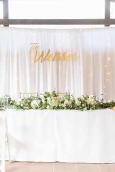 a table with flowers and greenery on it in front of a sign that says the wedding