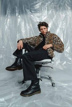 a man sitting on top of a chair in front of a white backdrop wearing black boots