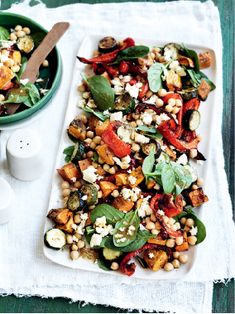 a white plate topped with salad next to a green bowl filled with beans and spinach