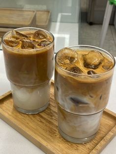 two glasses filled with iced coffee sitting on top of a wooden tray next to each other