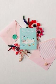 some pink envelopes and flowers on a white surface