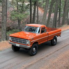 an orange pick up truck driving down a forest road