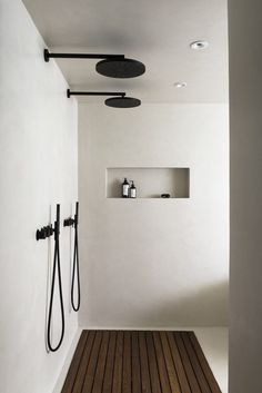 a white bathroom with wood flooring and black fixtures on the wall, along with two shower heads