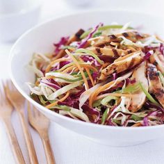 a white bowl filled with chicken, coleslaw and carrots next to wooden utensils