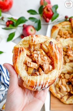 someone holding up a pastry with apples in the background