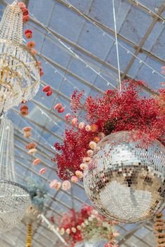 several chandeliers hanging from the ceiling with red flowers in them and one is disco ball