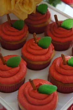 cupcakes with red frosting and green leaves on them sitting in a tray