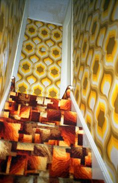 the carpeted stairs are lined with orange and yellow wallpaper, along with an intricate pattern