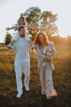 a man and woman are walking through the grass with two children on their shoulders,