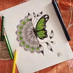 a drawing of a green butterfly on white paper with colored pencils next to it