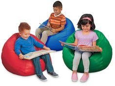 three children are sitting on bean bags reading books and looking at an open book in front of them