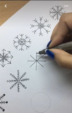 someone is drawing snowflakes on paper with a blue marker and some black ink