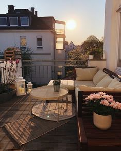 a balcony with couches, tables and potted flowers on the deck outside at sunset