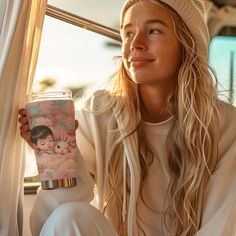 a woman sitting in front of a window holding a cup with an image on it