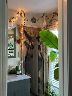 an open door leading to a bathroom with plants on the wall and curtains hanging from the ceiling