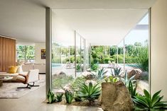 a living room filled with lots of plants next to a large stone statue in front of a glass wall