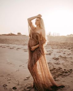 a woman standing on top of a beach next to the ocean wearing a long dress