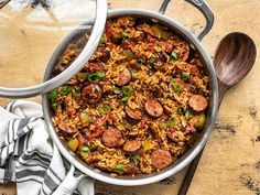 a pot filled with rice and sausage on top of a wooden table next to a spoon