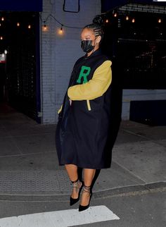 a woman wearing a face mask and black coat is walking down the street at night