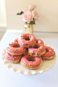 a plate full of donuts with pink frosting and sprinkles