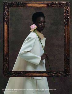 a woman holding a flower in front of a framed photo with the caption's name on it