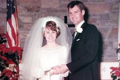 a man and woman standing next to each other in front of a brick wall with an american flag