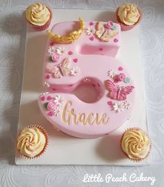 a pink birthday cake with cupcakes around it and the number five on top