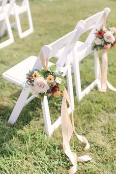 two white wooden benches with flowers and ribbons tied to the back, sitting on grass