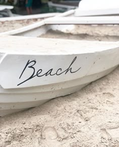 a white boat with the word beach written on it's side sitting in the sand