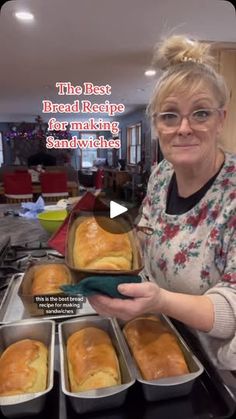 a woman holding trays of bread on top of a kitchen counter in front of pans