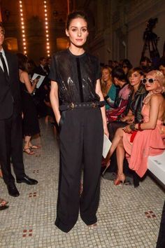 a woman standing in front of a crowd at a fashion show wearing black pants and heels