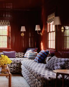 a living room filled with lots of furniture next to two large windows and wooden paneled walls