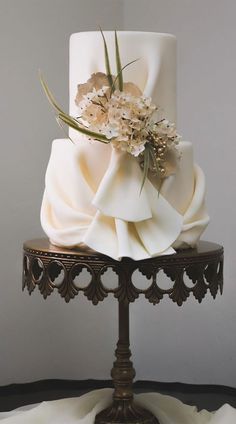 a three tiered wedding cake with white flowers on top and gold trimmings