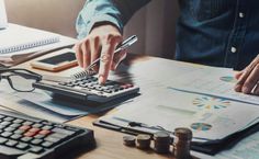 a person is using a calculator at a desk with stacks of coins and papers