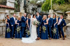 a bride and groom with their bridal party in front of an old stone fountain