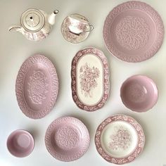 an assortment of pink and white plates, teapots and saucers on a table