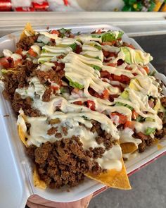 a person holding a tray with nachos covered in sauce and toppings on it