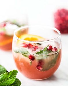 two glasses filled with drinks and garnished with mint, lemon, and pomegranate