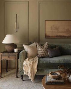 a living room with green couches and pillows on top of the couch, next to a lamp