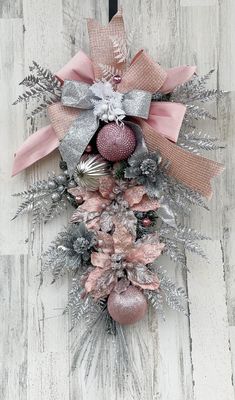 a pink and silver christmas wreath on a white wooden wall with ornaments hanging from it