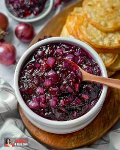 a bowl filled with cranberry sauce next to crackers on a cutting board