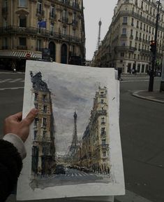 a person holding up a drawing in front of some buildings