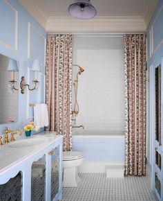 a bathroom with blue walls, white fixtures and floral curtained drapes on the windows